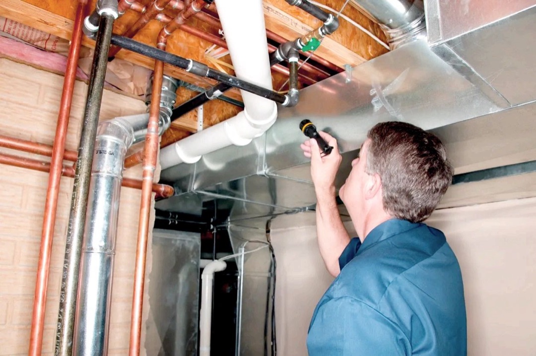 Islam Jaber inspecting exposed pipes and ductwork with a flashlight